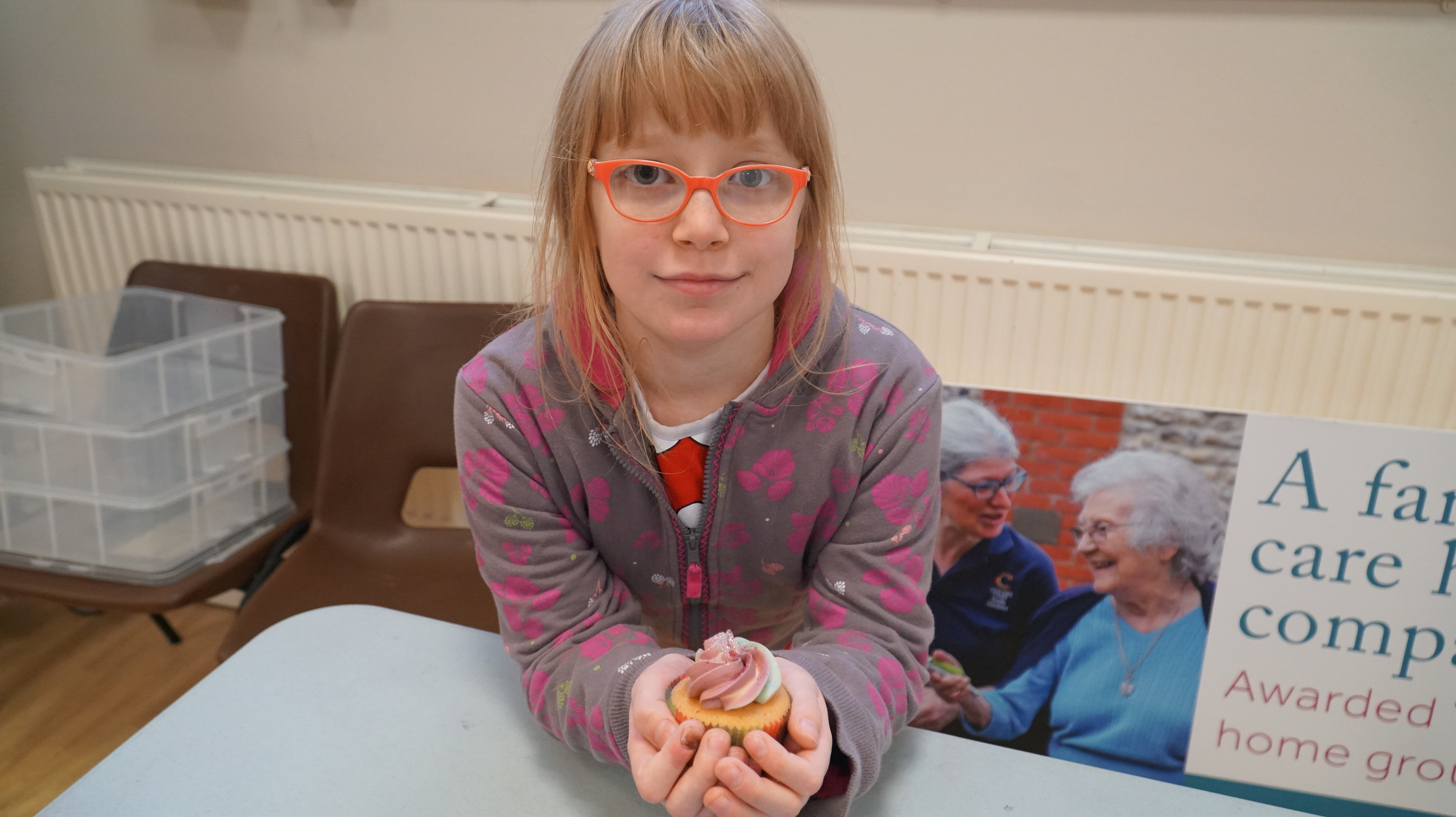  A child wearing orange glasses, holding a cup cake in their hands 